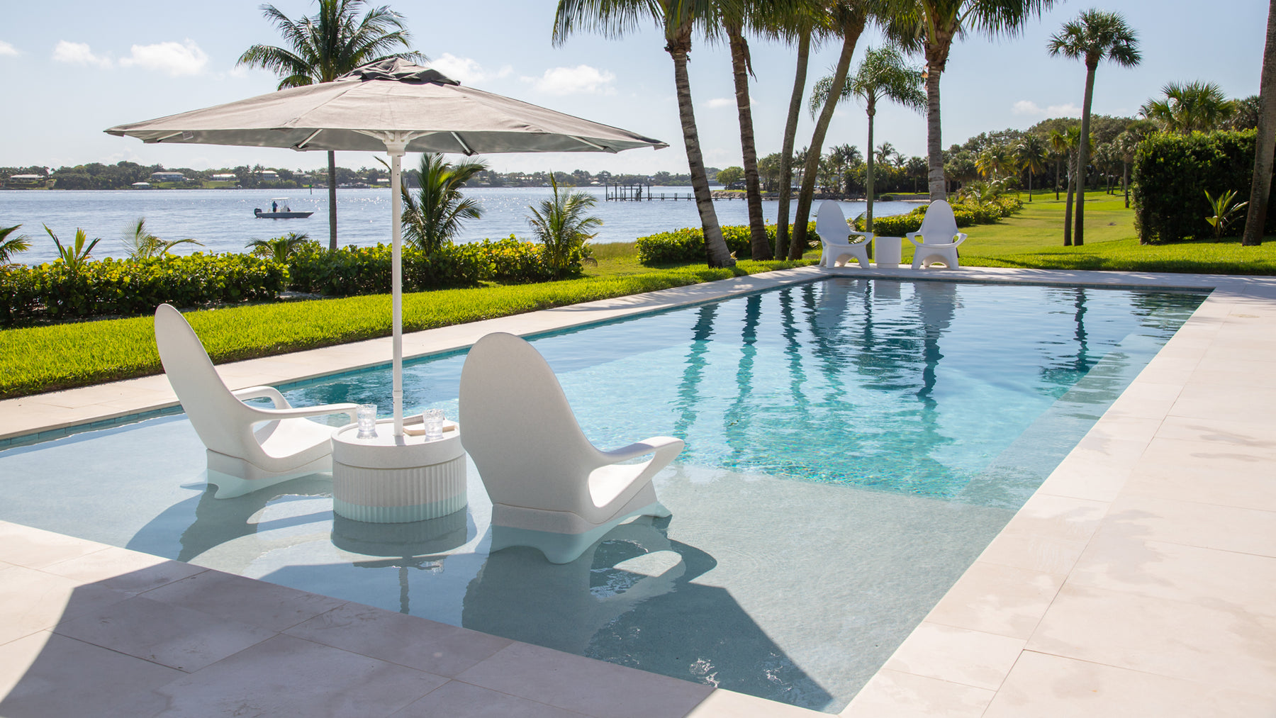 A modern pool deck with white tanning ledge chairs and in-pool side table with umbrella hole.