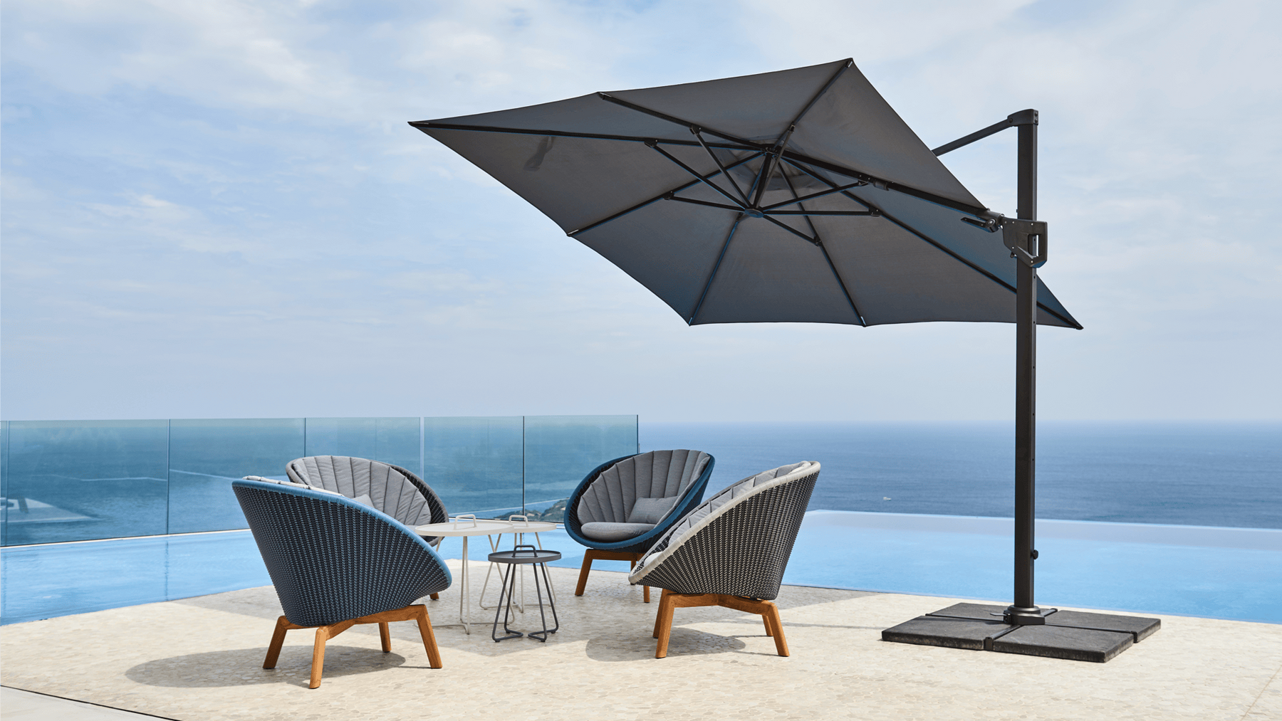 A large cantilever umbrella shades 4 high-backed chairs on a seaside patio.