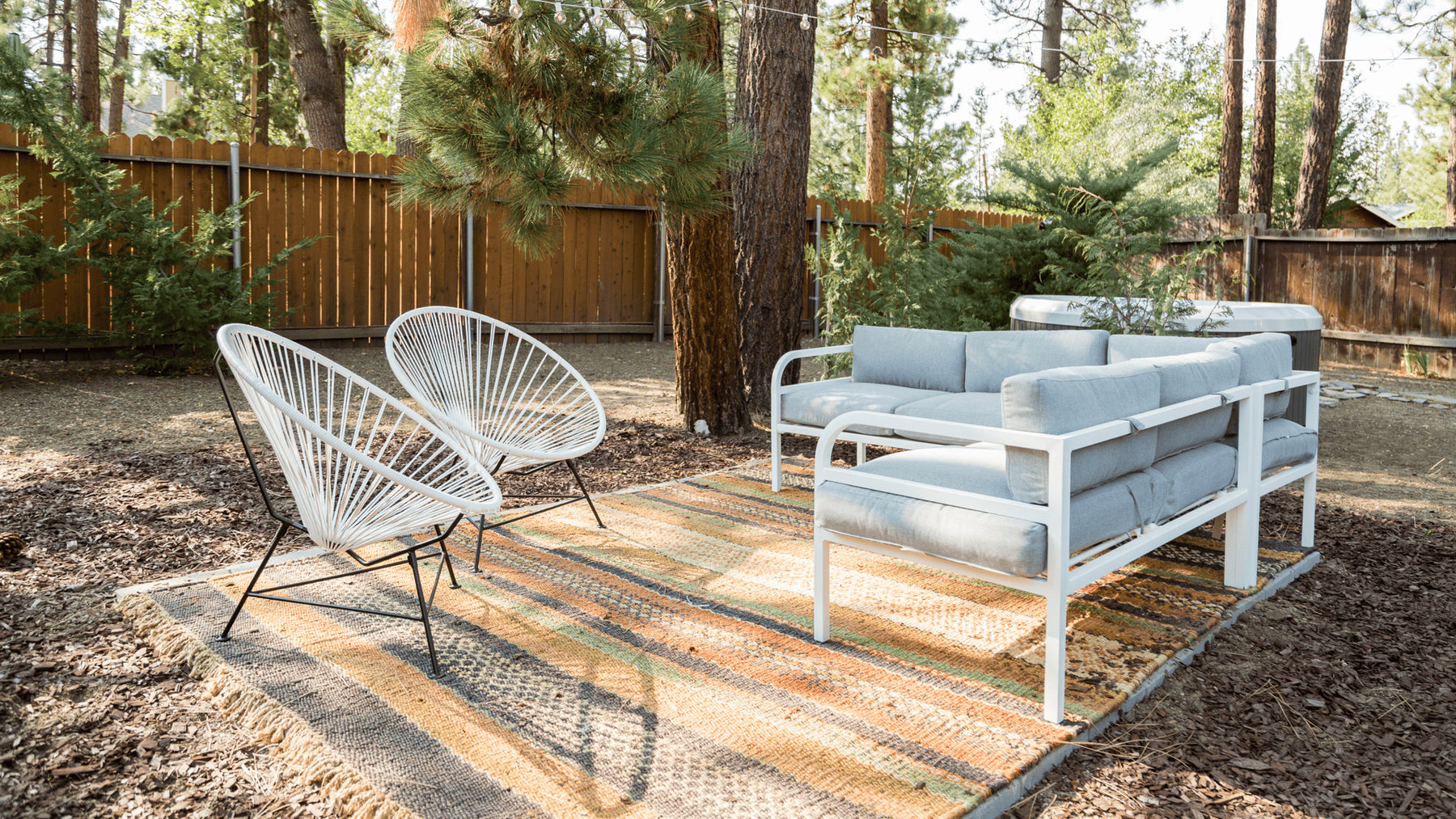 A wooded patio area featuring white Luna outdoor chairs, an outdoor a rug, and sectional.