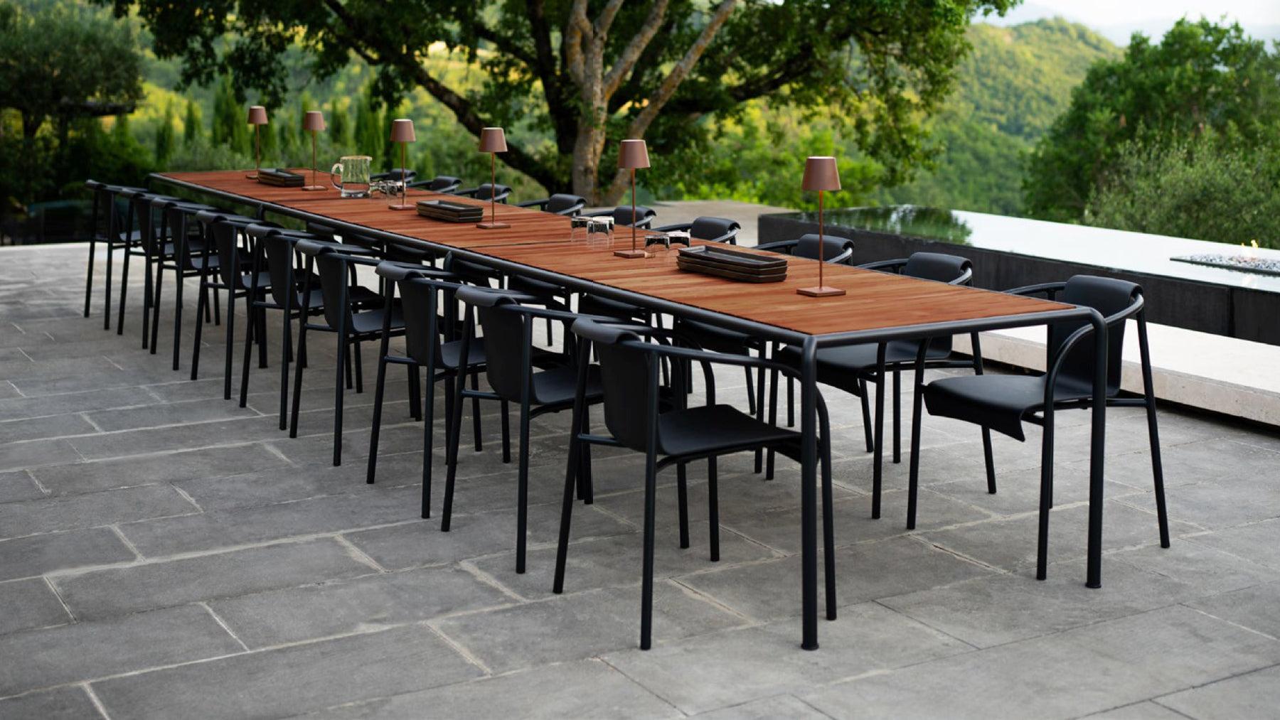 A long banquet table with dark wood top and black metal frame accompanied by matching black metal round-back chairs.