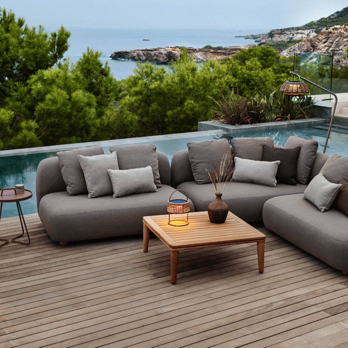 An outdoor lounge area beside a pool is illuminated with outdoor candles and a woven table lamp.