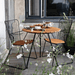 A round outdoor coffee table with bamboo lamella top and 2 outdoor dining armchairs with bamboo lamella seat set on a wooden deck patio