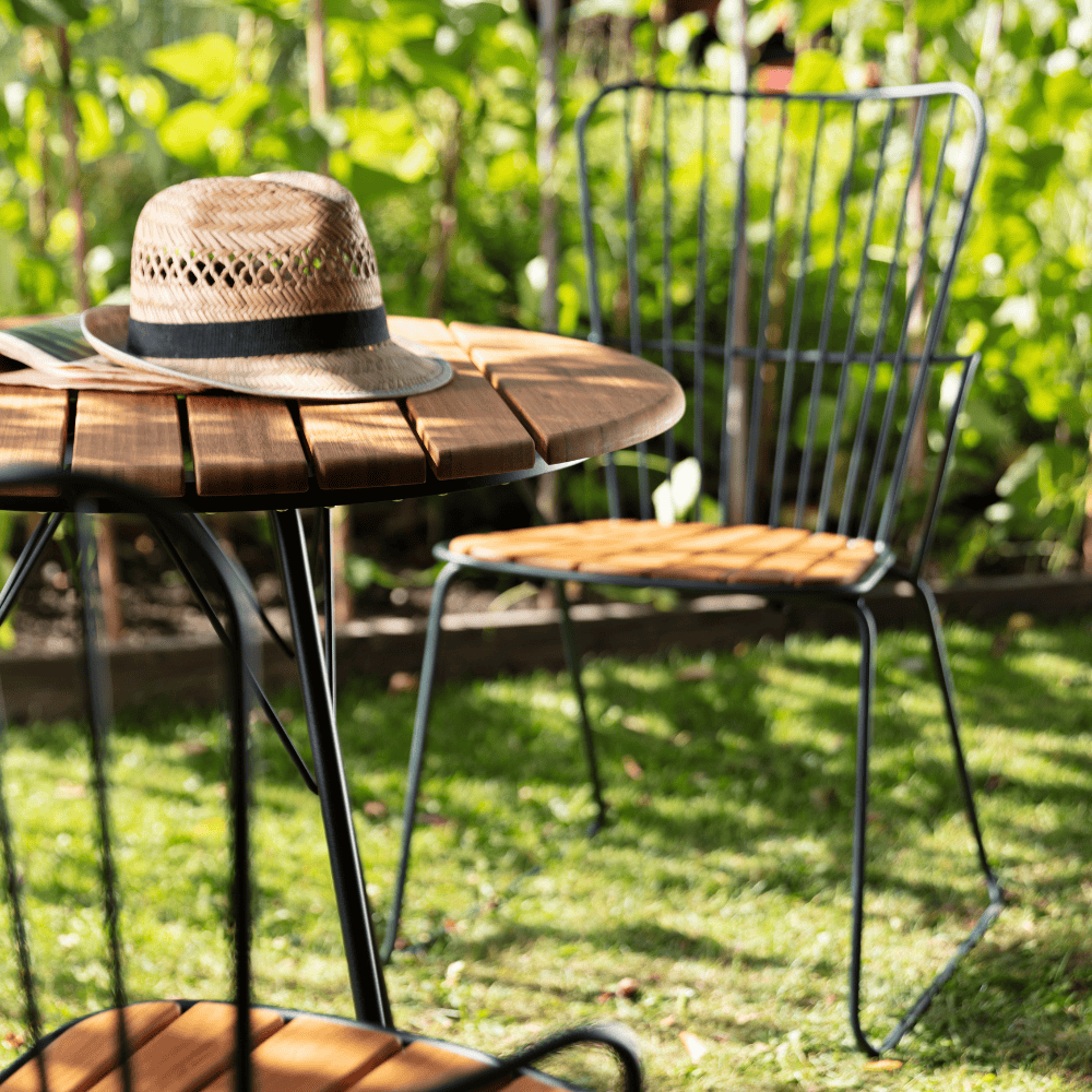 Close up view of round outdoor coffee table with bamboo lamella top with brown hat on top placed on a lawn area