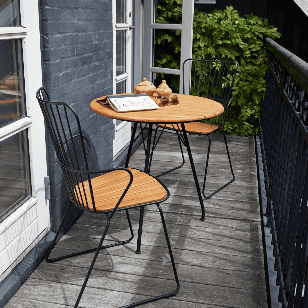 A round outdoor coffee table with bamboo lamella top with 2 outdoor dining chairs set on a wooden deck balcony