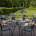 An outdoor seating area with several black round outdoor coffee tables and black outdoor dining armchairs near grassy field