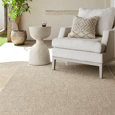 A light beige machine woven outdoor rug placed on a patio with white outdoor lounge chair, a white side table 