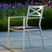 A white aluminum stackable outdoor dining armchair with padded wicker placed on a patio near plants with purple flowers