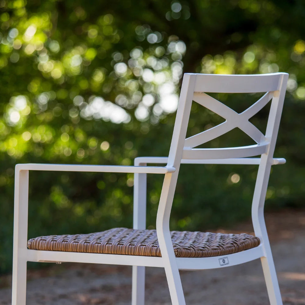 White aluminum stackable outdoor dining armchair with padded wicker placed on an outdoor area with plants and trees