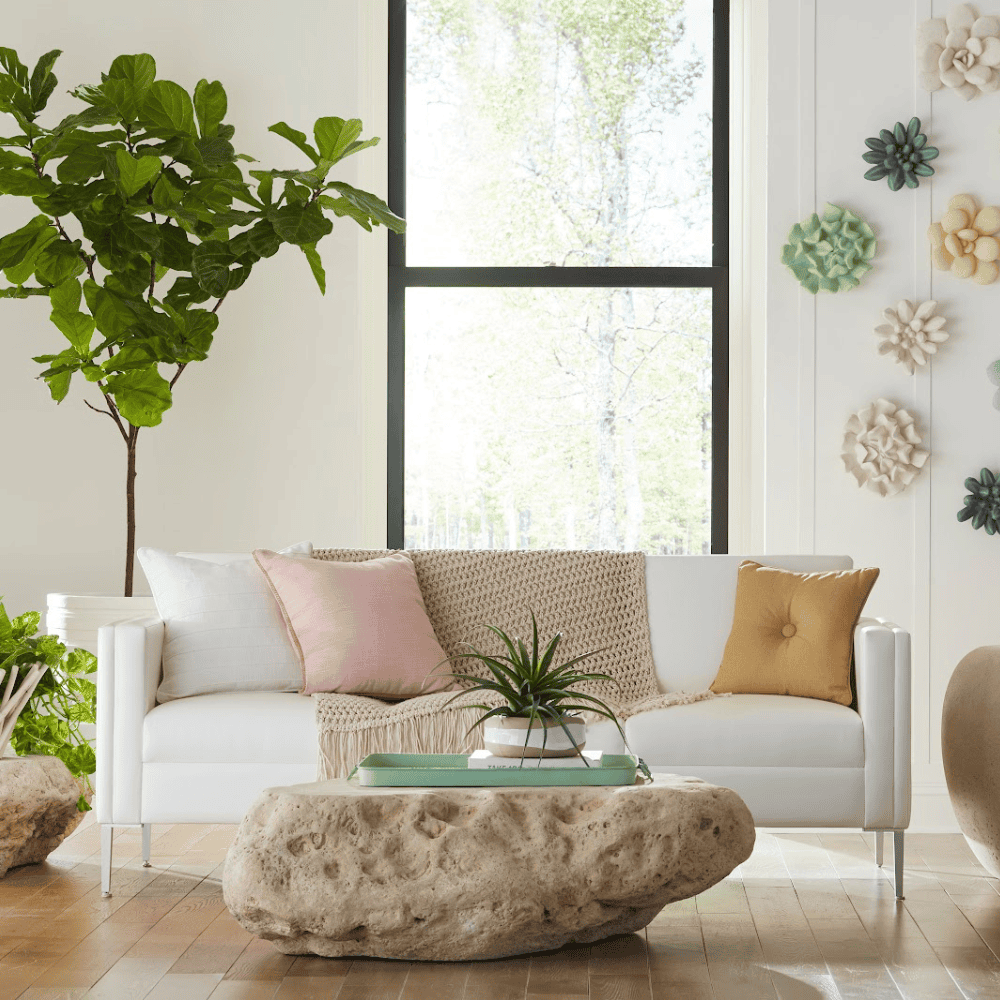 Organic shaped concrete pebble outdoor coffee table on a wooden deck indoor setting with white sofa and potted plants