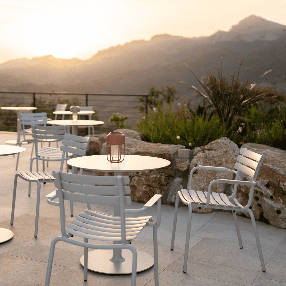 Outdoor seating area with white stackable outdoor dining chairs and round outdoor dining tables beside rocks and greenery