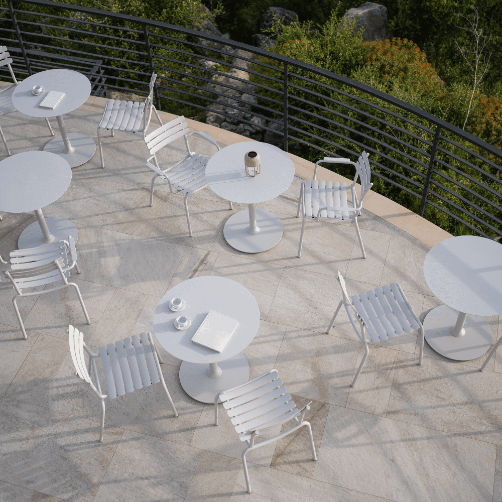 Multiple set of white stackable outdoor dining chairs and white round outdoor dining tables set on a tiled outdoor patio