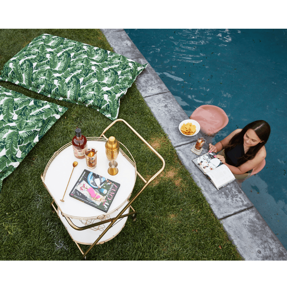 Pool barstool in a coral color placed in a pool with a woman sitting on it and 2 green white pool pillow