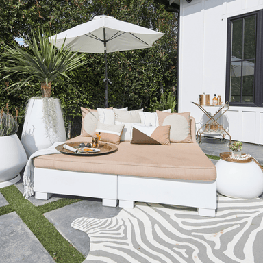 big white modern umbrella mounted beside large sun bed with pillows on it placed on the patio