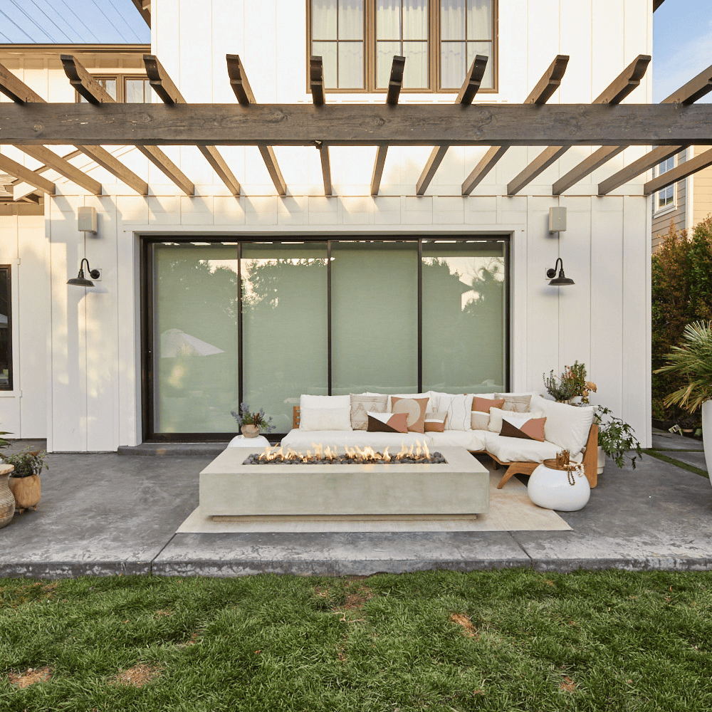 A white concrete outdoor rectangular fire pit table and white outdoor sectional sofa with teak frame set on a stylish patio