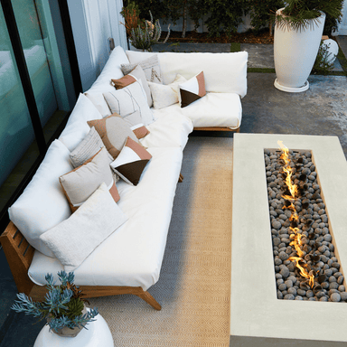 White outdoor sectional sofa with teak frame and pillows  placed on a patio accompanied by a rectangular fire table