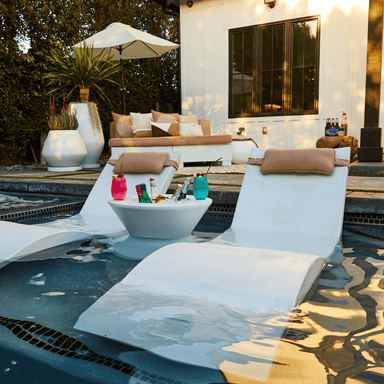 white outdoor concrete planter placed beside the pool with 2 white chaise lounge and a white pool side table in the pool