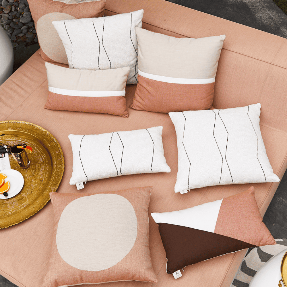 variety of decorative ebony pillows on white and beige color together with golden tray arranged on a beige outdoor sofa 