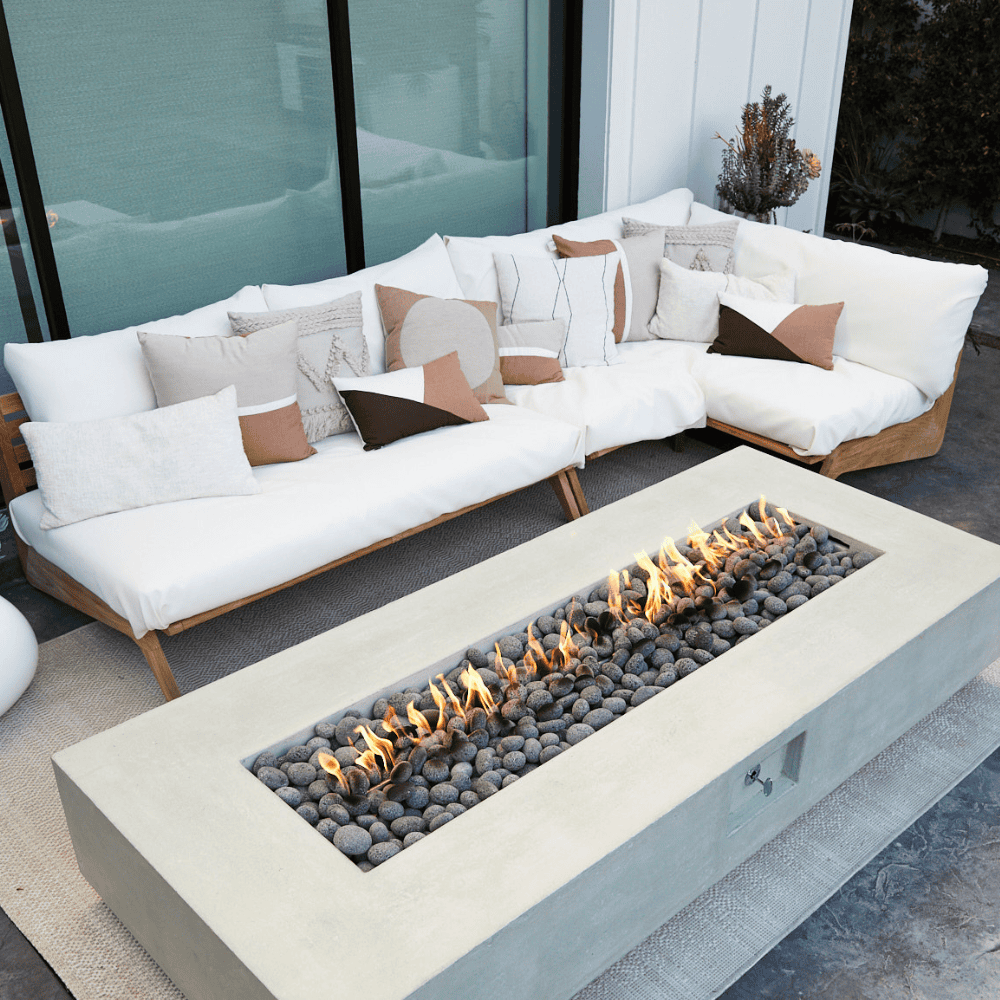 A white concrete outdoor rectangular fire pit table and white outdoor sectional sofa with teak frame set on an outdoor patio