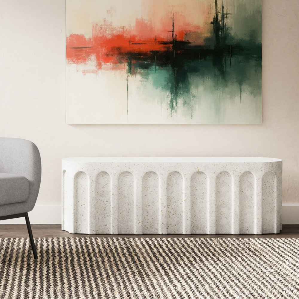 A white outdoor concrete oval bench with arched design pattern set in a living room against white wall with abstract painting