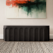 A matte black outdoor concrete oval bench with arched design pattern set in a living room against white wall with abstract painting