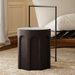 A round outdoor concrete round stool in matte black color placed in a living room beside cushioned lounge chair