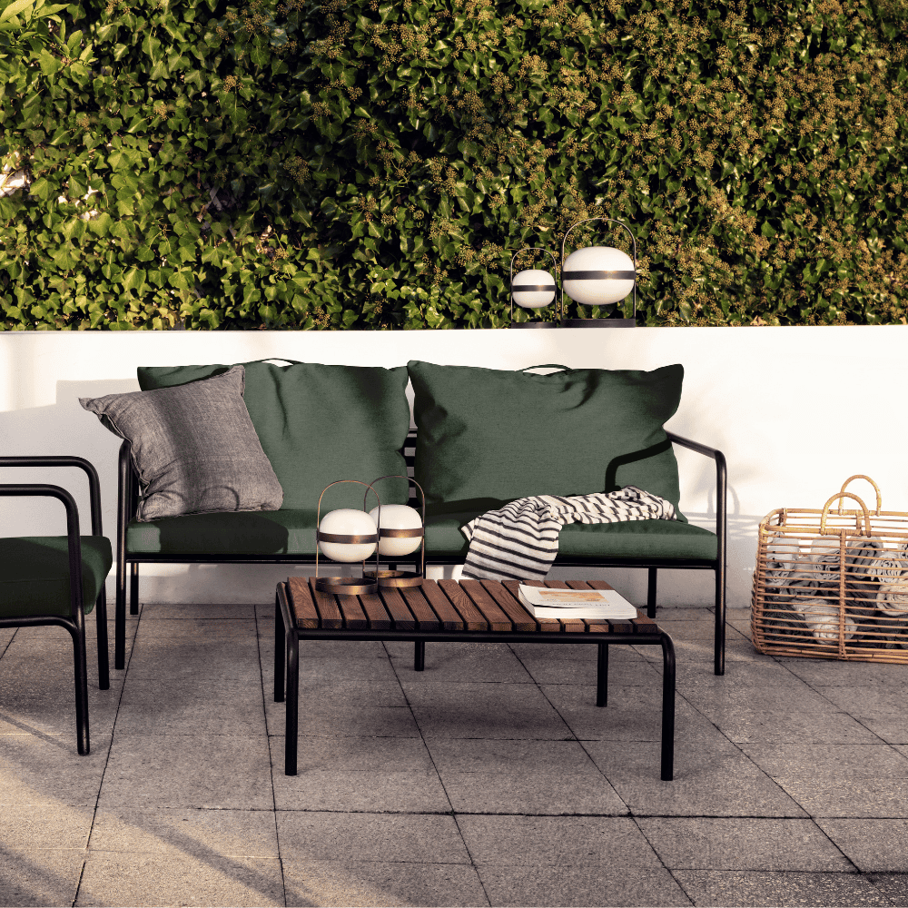 A wooden outdoor lounge table with black metal frame and dark green outdoor lounge sofa and chair set on a tiled patio