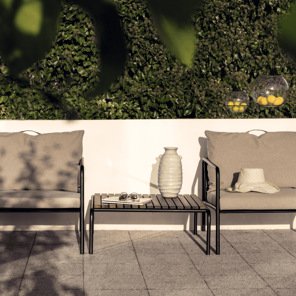 A wooden outdoor lounge table with black metal frame and 2 beige outdoor lounge chairs set on a tiled patio