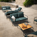 A patio area with wooden outdoor lounge table with black metal frame and several dark green outdoor lounge sofa and chairs