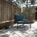 A dark green outdoor lounge chair with black aluminum frame placed on a wooden deck patio beside of bamboo fence under a tree