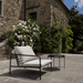 White outdoor lounge chair with black aluminum frame and black round metal outdoor tray table set on a patio near the stairs