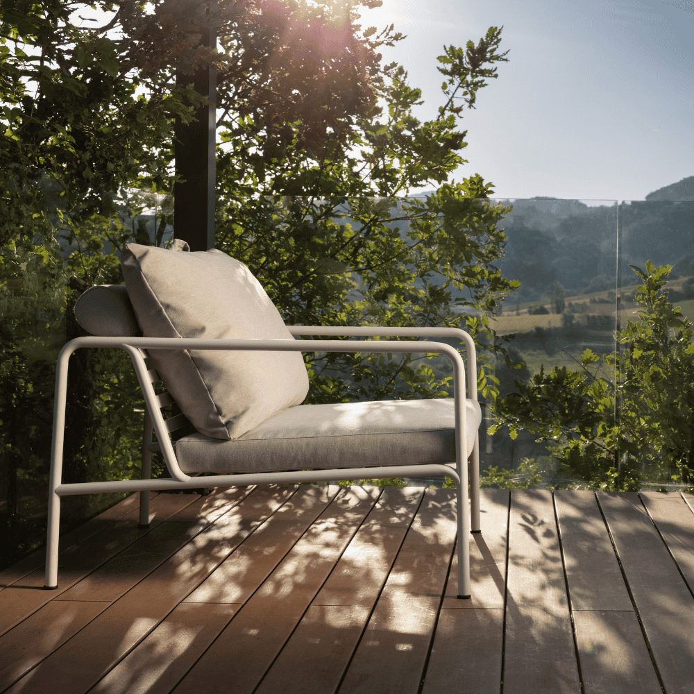 A white outdoor lounge chair placed on a wooden deck patio surrounded by plants