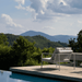 A white outdoor lounge chair placed beside the pool surrounded by trees with a view of a distant mountains