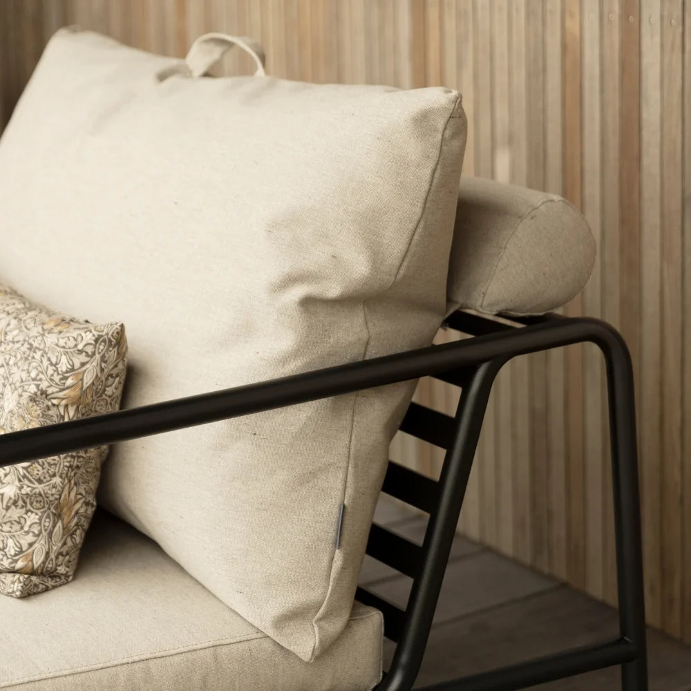 Close up view of a beige outdoor lounge chair with black aluminum frame set against wooden wall