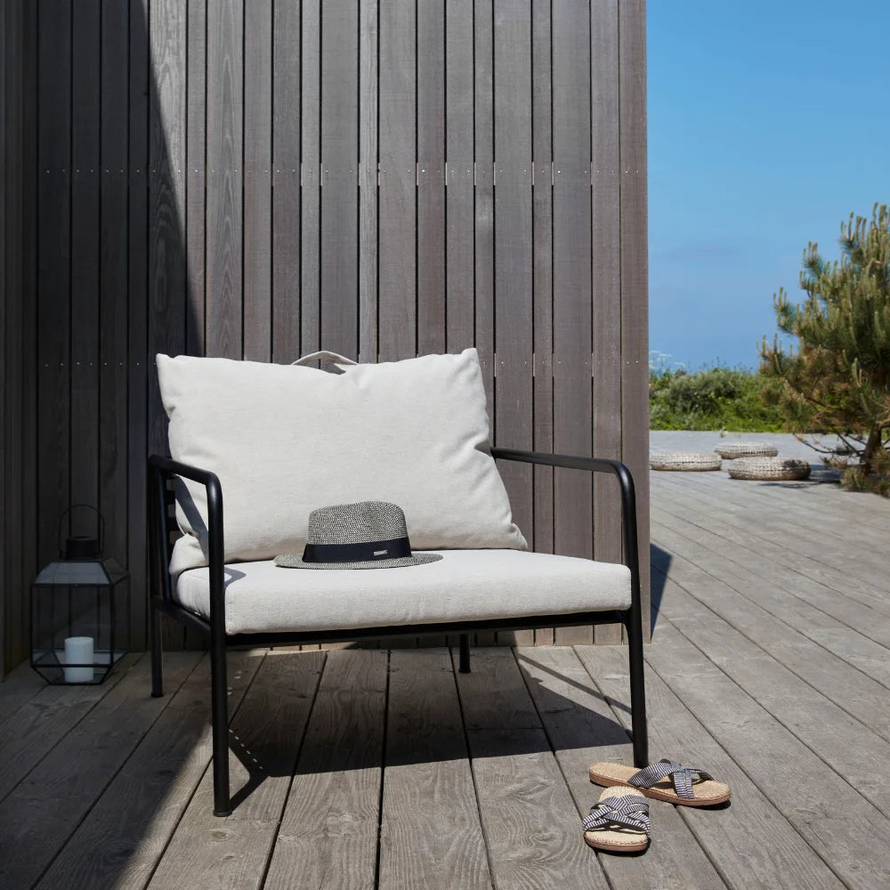 A white outdoor lounge chair with black aluminum frame set on a wooden deck patio against wooden wall