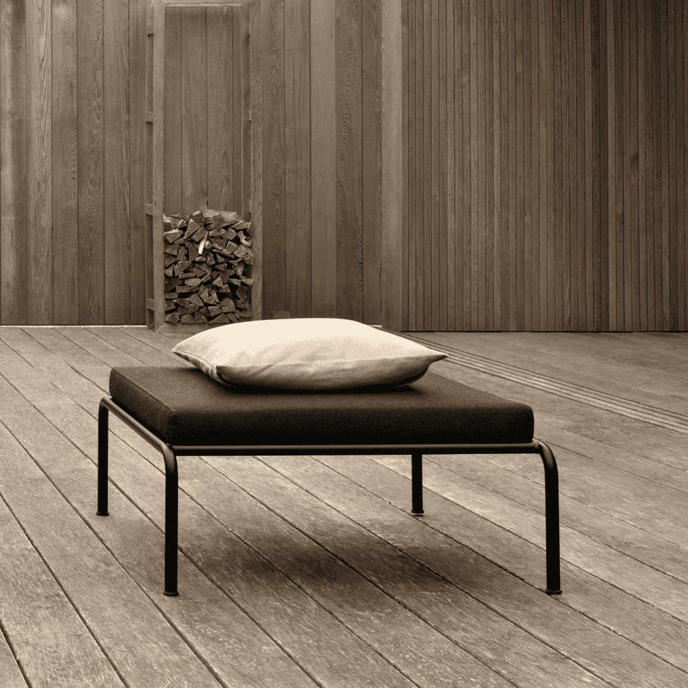 A wooden deck patio featuring a black outdoor ottoman with black aluminum frame with pillow on top 