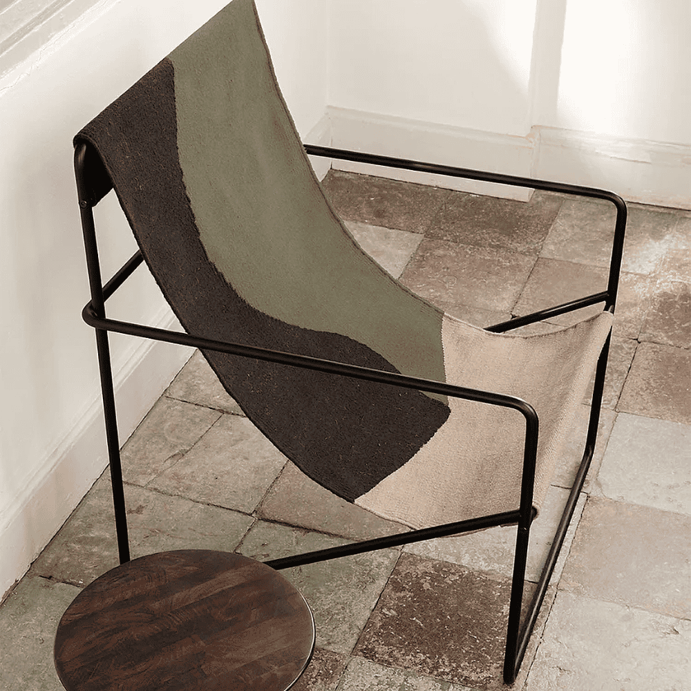 black and olive green outdoor lounge chair with black steel frame placed on a tiled floor beside small round wooden table