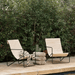 modern beige outdoor lounge chair with black steel fame placed on a concrete poolside surrounded by plants