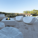 Two white moon Shaped pool chairs placed on a patio together with a concrete fire table and L shaped white outdoor Sofa