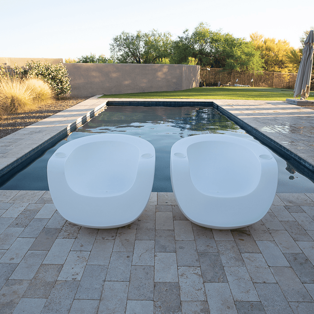 Two white moon Shaped pool chairs placed on a patio together with a concrete fire table and L shaped white outdoor Sofa