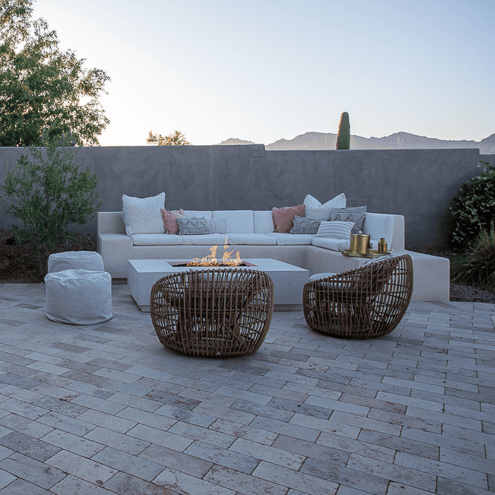 White concrete rectangular fire pit on a patio surrounded by L shaped white sofa, wicker chairs and fabric footstool