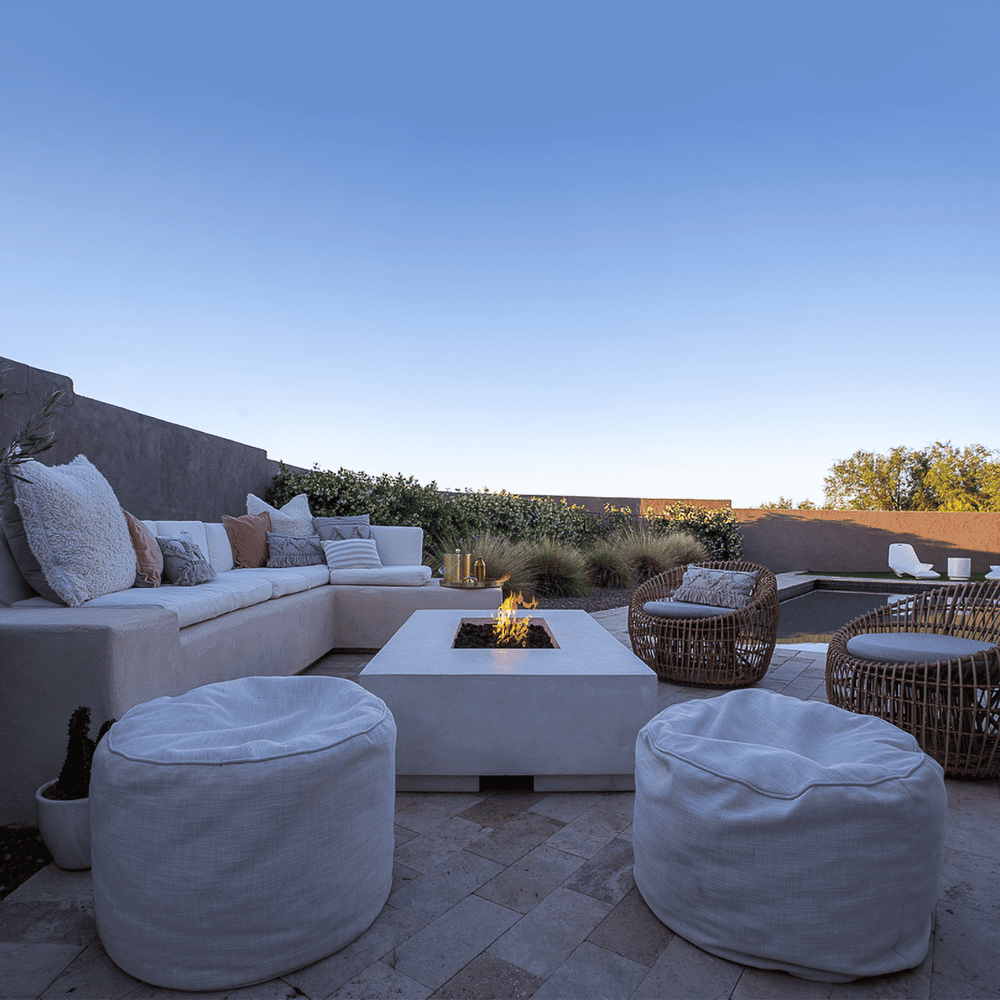 White concrete rectangular fire pit on a patio beside the pool with L shaped white sofa, wicker chairs and fabric footstool