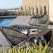 A black concrete outdoor rectangular fire pit table with black Acapulco chair and loveseat set on a patio beside the pool