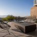 A black concrete outdoor rectangular fire pit surrounded by Acapulco chairs and loveseat set on a patio beside the pool