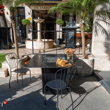 Black square outdoor dining table fire table pit set on a modern outdoor patio setting beside of two small palm trees