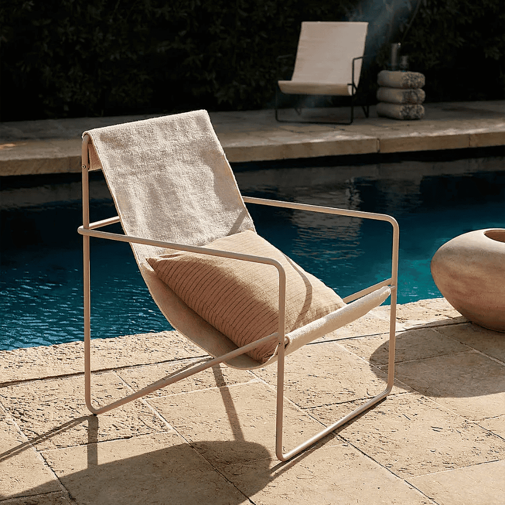 modern outdoor lounge chair in beige color with light brown steel frame set beside the pool with brown pillow on it