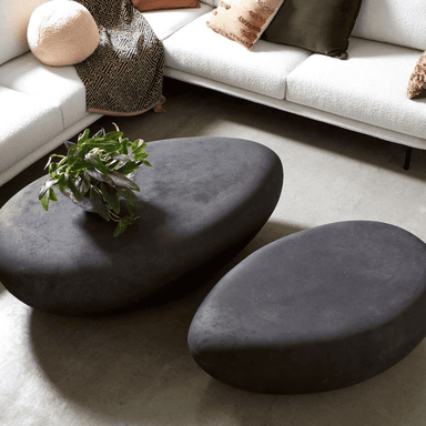 Two charcoal pebble coffee table in different sizes sets on a modern living room with two white sofa and pillows on it