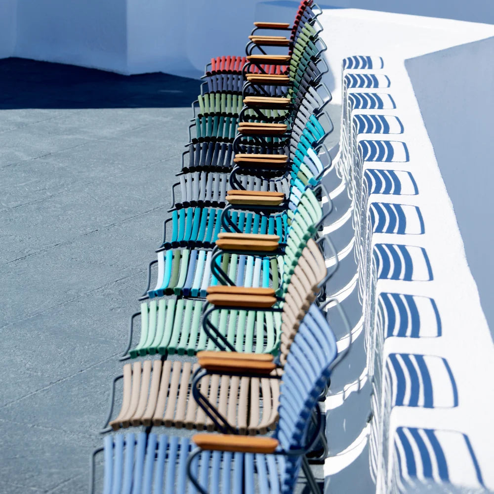 A row of colorful outdoor dining chairs tall back with bamboo armrest placed on an outdoor area against white wall