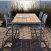 4 gray outdoor dining chair tall back and wooden rectangular outdoor dining table set on a wooden deck beside tall grass