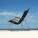 A dark green outdoor lounge chair with bamboo armrest placed on a white surface under a blue sky