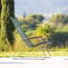 A green outdoor lounge chair with bamboo armrest placed on an outdoor area beside grassy field